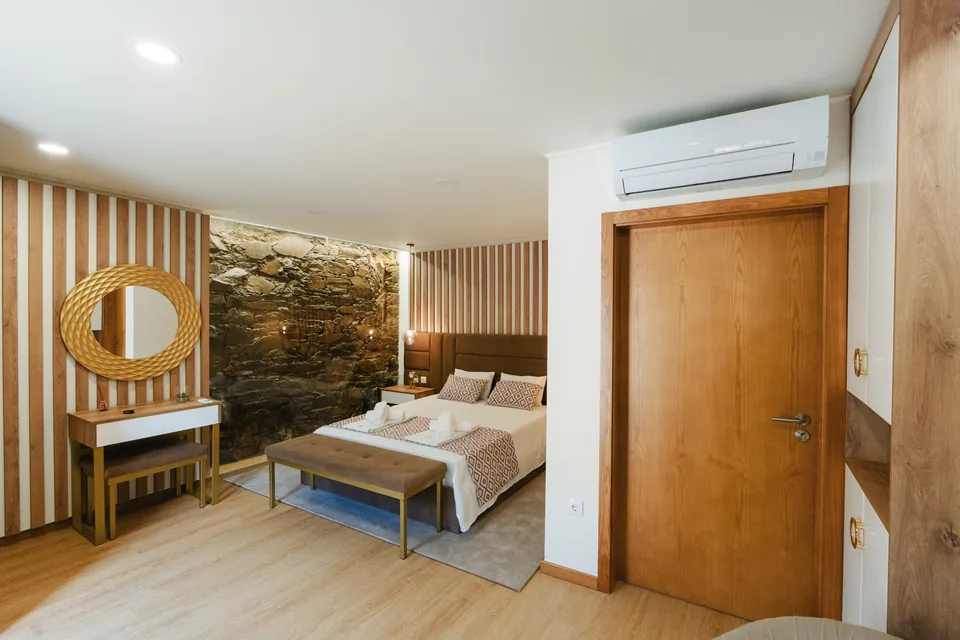 Suite double bed, exposed stone wall, timber slats and bathroom doorway