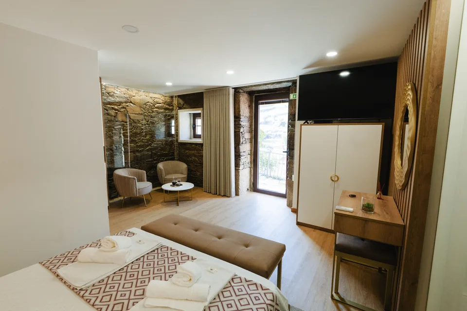 Suite from bed towards chairs, doors, television and stone wall
